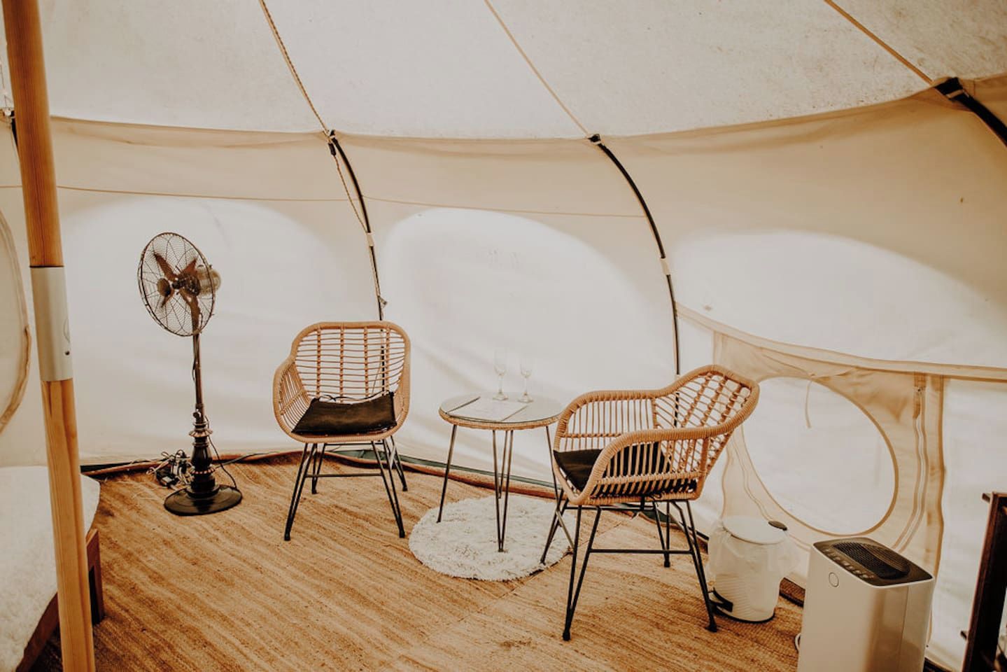 A tent with two wicker chairs, a small table, a fan, and a portable heater.