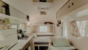 Ein kompaktes Wohnmobil-Interieur mit einer Küchenzeile, einem kleinen Bett und einem Fenster mit Vorhängen.