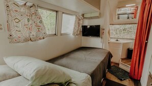 Ein kleines Zimmer mit einem Bett, einem Fernseher, einem kleinen Fenster und einem Waschbecken.