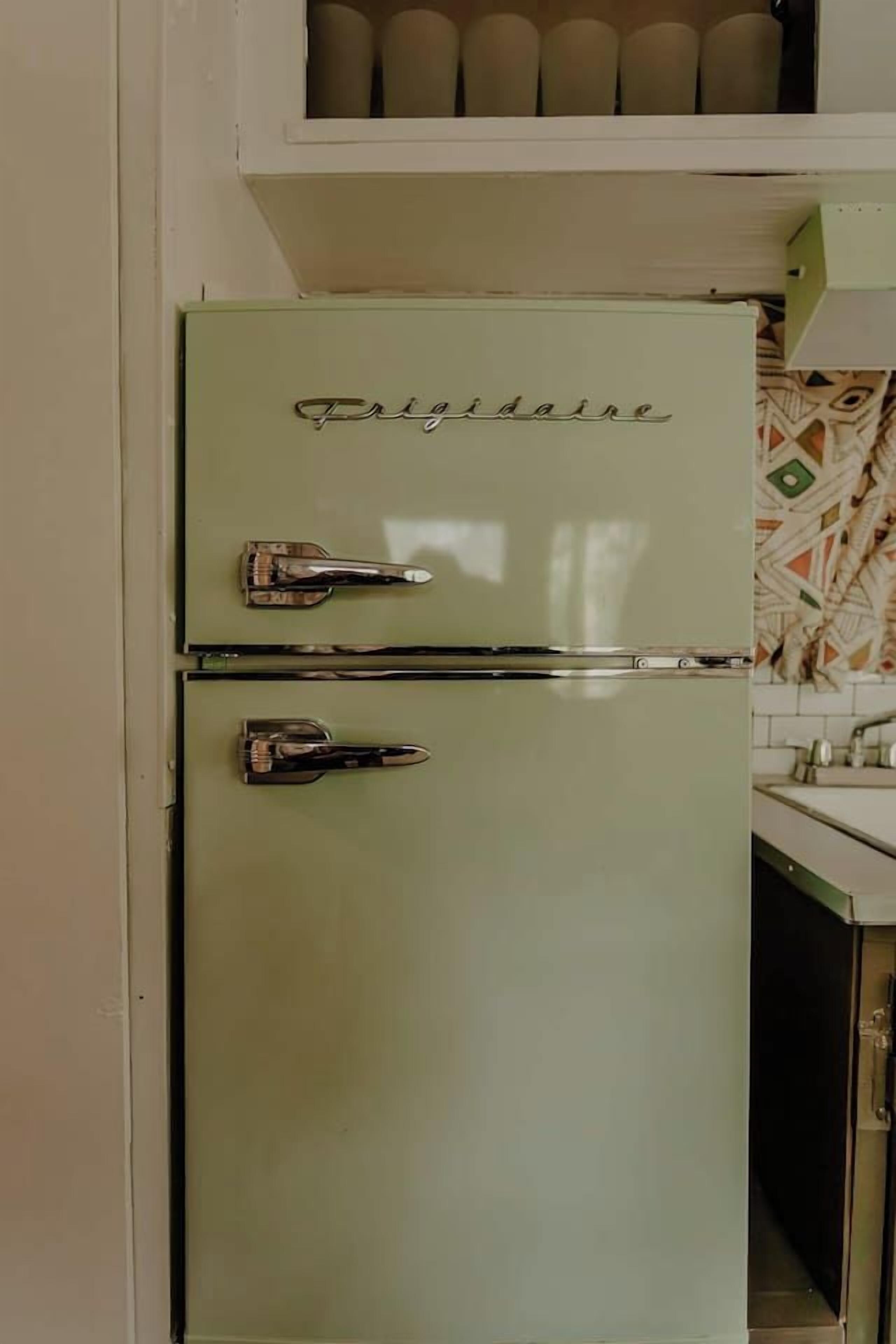 A vintage refrigerator with two doors, a lower freezer, and a top storage compartment.