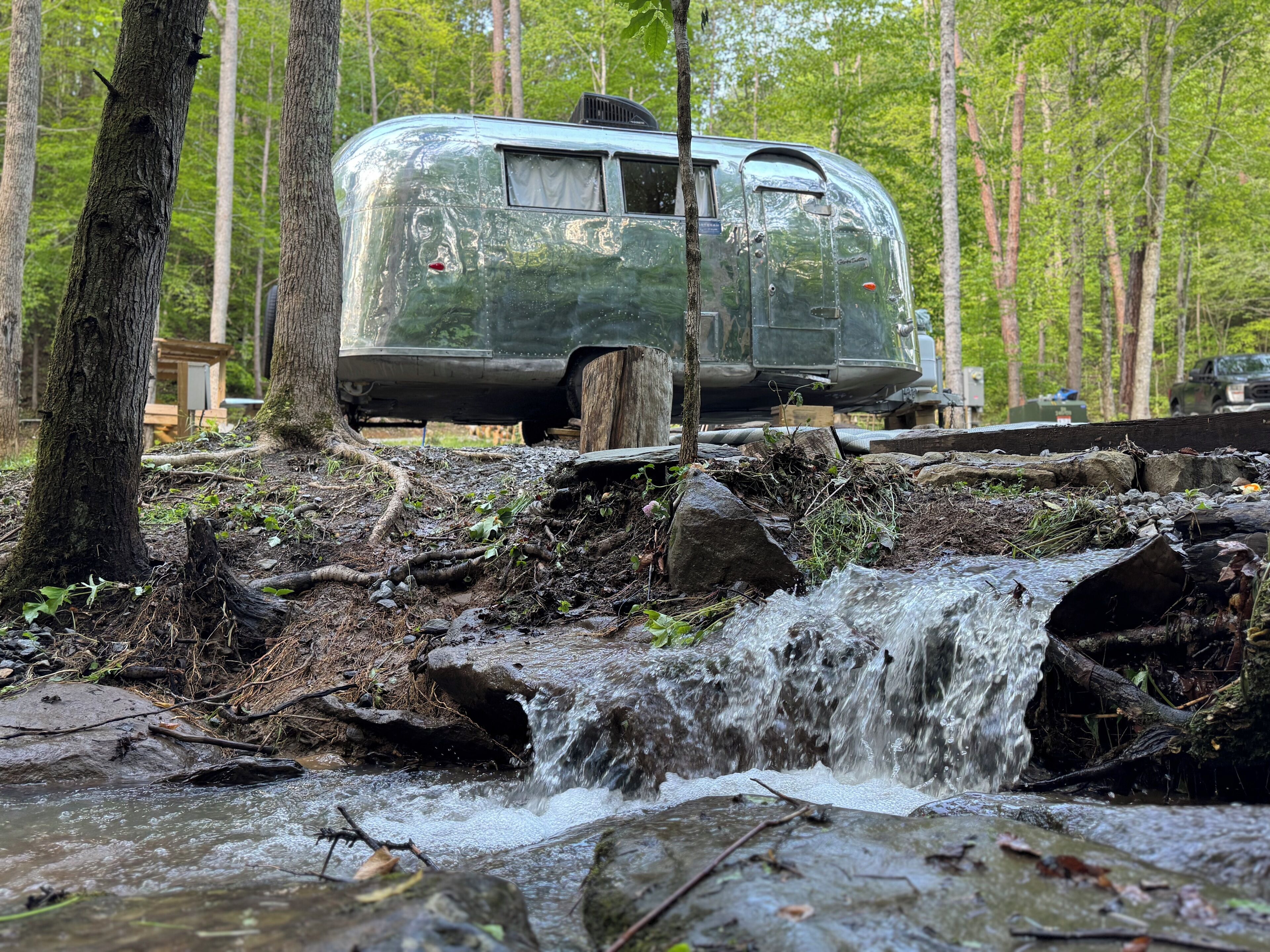 Een oude camper staat bij een kleine waterval in een bebost gebied.