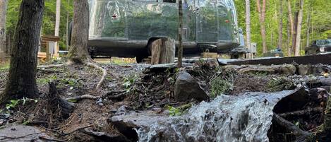 Een oude camper staat bij een kleine waterval in een bebost gebied.