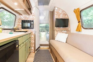 Un intérieur de camping-car compact comprenant un coin cuisine, un téléviseur fixé au mur et un canapé avec un coussin.