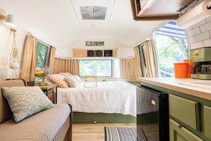 Un intérieur de camping-car compact comprenant un lit, un coin cuisine et une fenêtre donnant sur l’extérieur.