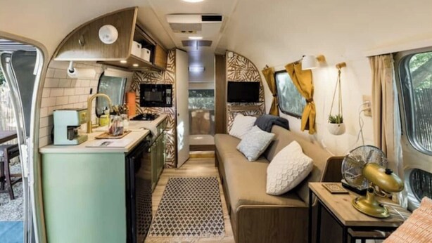 A compact RV interior with a kitchenette, a sofa, and a TV. - Creekside Airstream Retreat in the Smokies (Cosby)