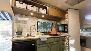 A compact kitchen with a microwave, coffee maker, and storage cabinets. - Creekside Airstream Retreat in the Smokies (Cosby)