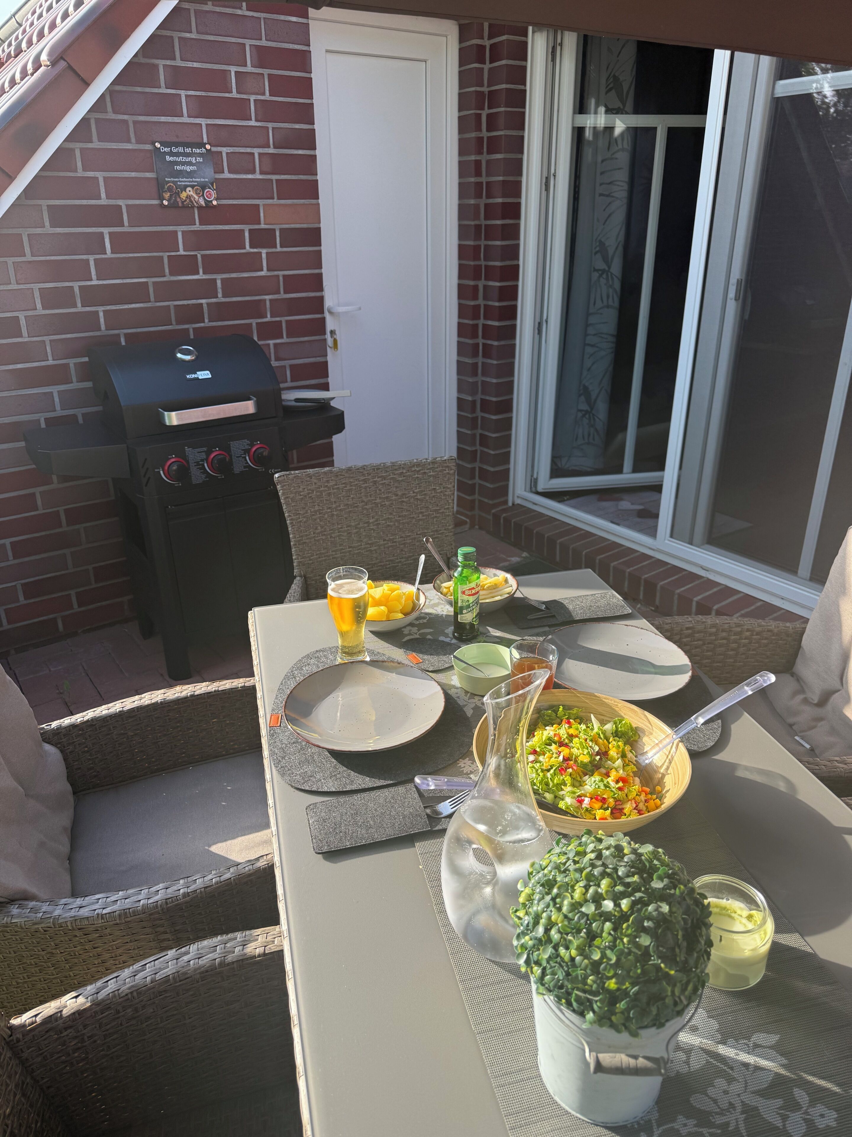 En uteplats med en grill, ett matbord, stolar och ett fönster.