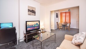 A living room with a flat-screen TV, a glass coffee table, a sofa, a dining area with a table and chairs, and a door leading to another room. - Captivating 3-bed House in Central Doncaster (Doncaster)