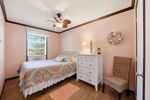Ein Schlafzimmer mit Bett, Schminktisch, Stuhl, Fenster und Deckenventilator.