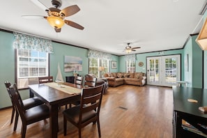 A spacious living area with a dining table, chairs, a sofa, and ceiling fans.