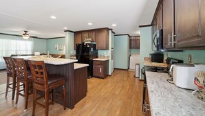 Una cocina con armarios de madera, una isla central, taburetes de bar, un refrigerador, una estufa y un microondas.