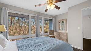 Un dormitorio con una cama grande, ventilador de techo, cómoda y ventana con vistas a árboles.
