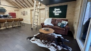 Interior acogedor de una cabaña con techo de madera, comedor con refrigerador rojo, sofá de cuero marrón y alfombra de piel de vaca.