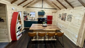 Interior acogedor de una cabaña de madera, con cocina, una mesa de comedor y cuatro sillas, además de un refrigerador rojo.