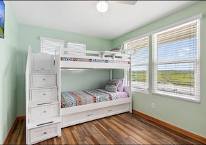 Un lit superposé avec des tiroirs, une fenêtre avec des stores et une vue sur l’extérieur.