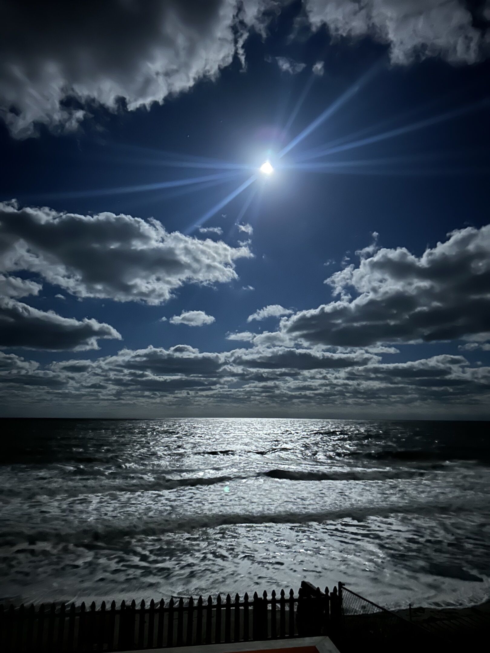 Blick auf das Meer mit Wellen und einem Zaun im Vordergrund.