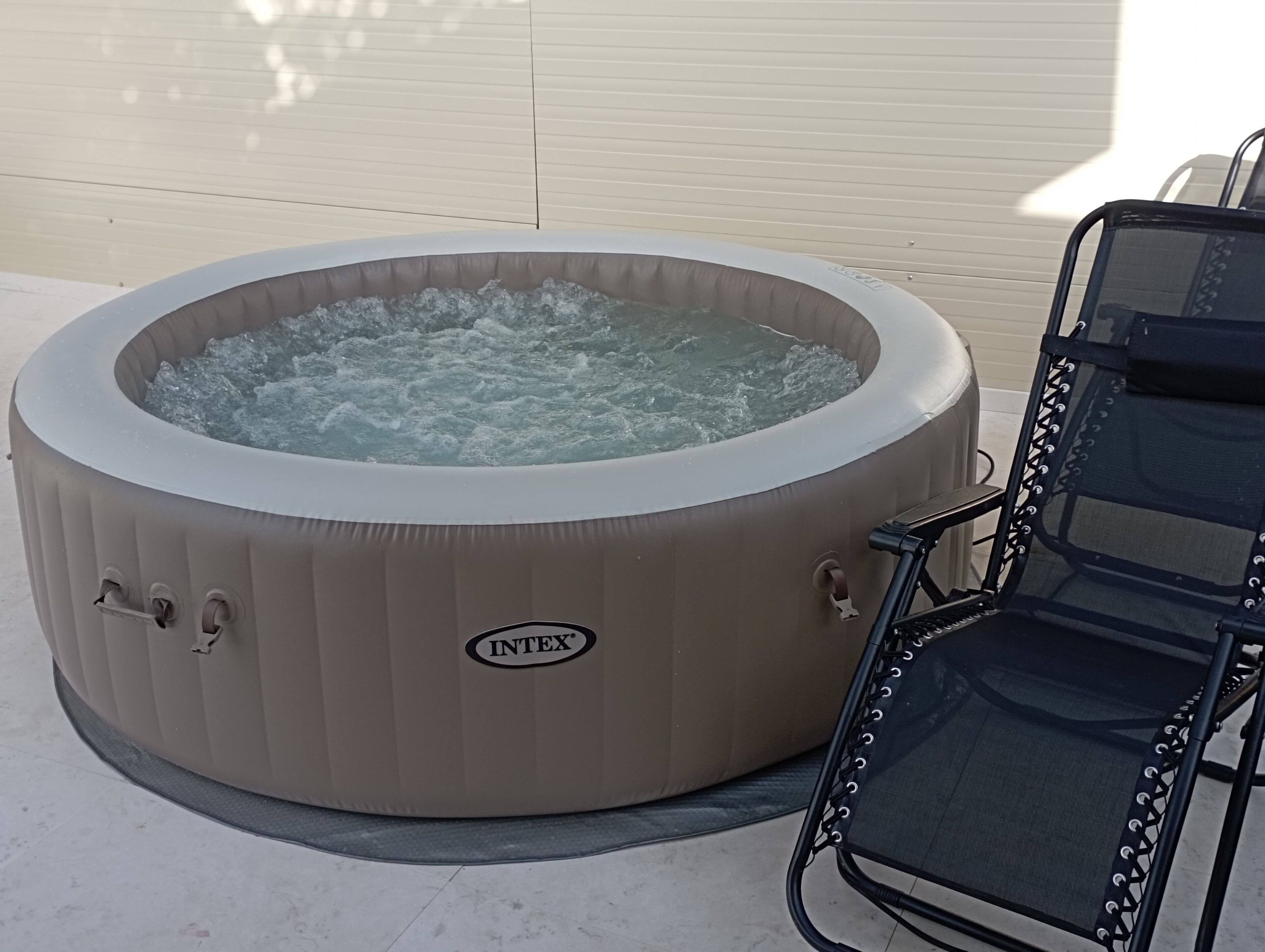 A hot tub with a brand name visible, placed outdoors next to a chair.