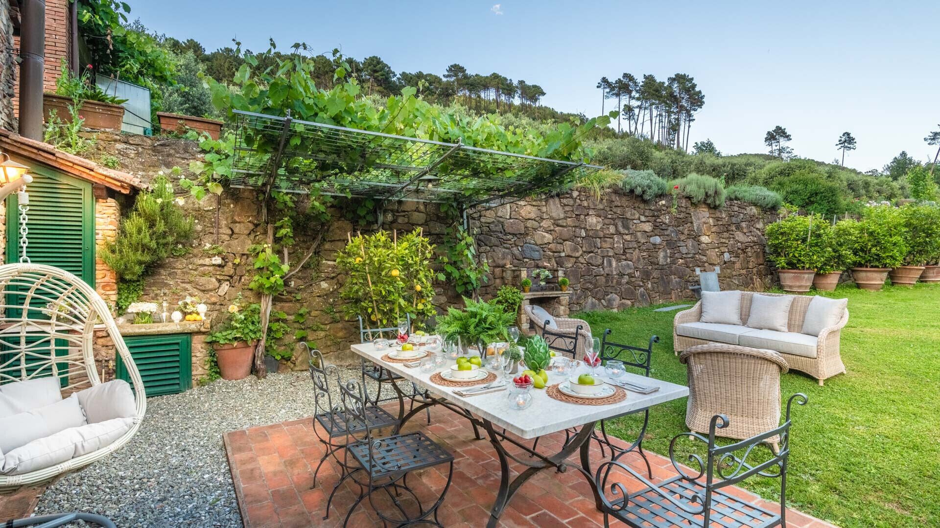 Un patio al aire libre con una mesa lista para comer, rodeado de mobiliario de mimbre y plantas en macetas.