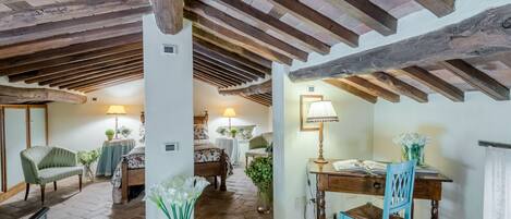 A rustic room with exposed wooden beams, a wooden desk, a chair, a bed, and a table with lamps.