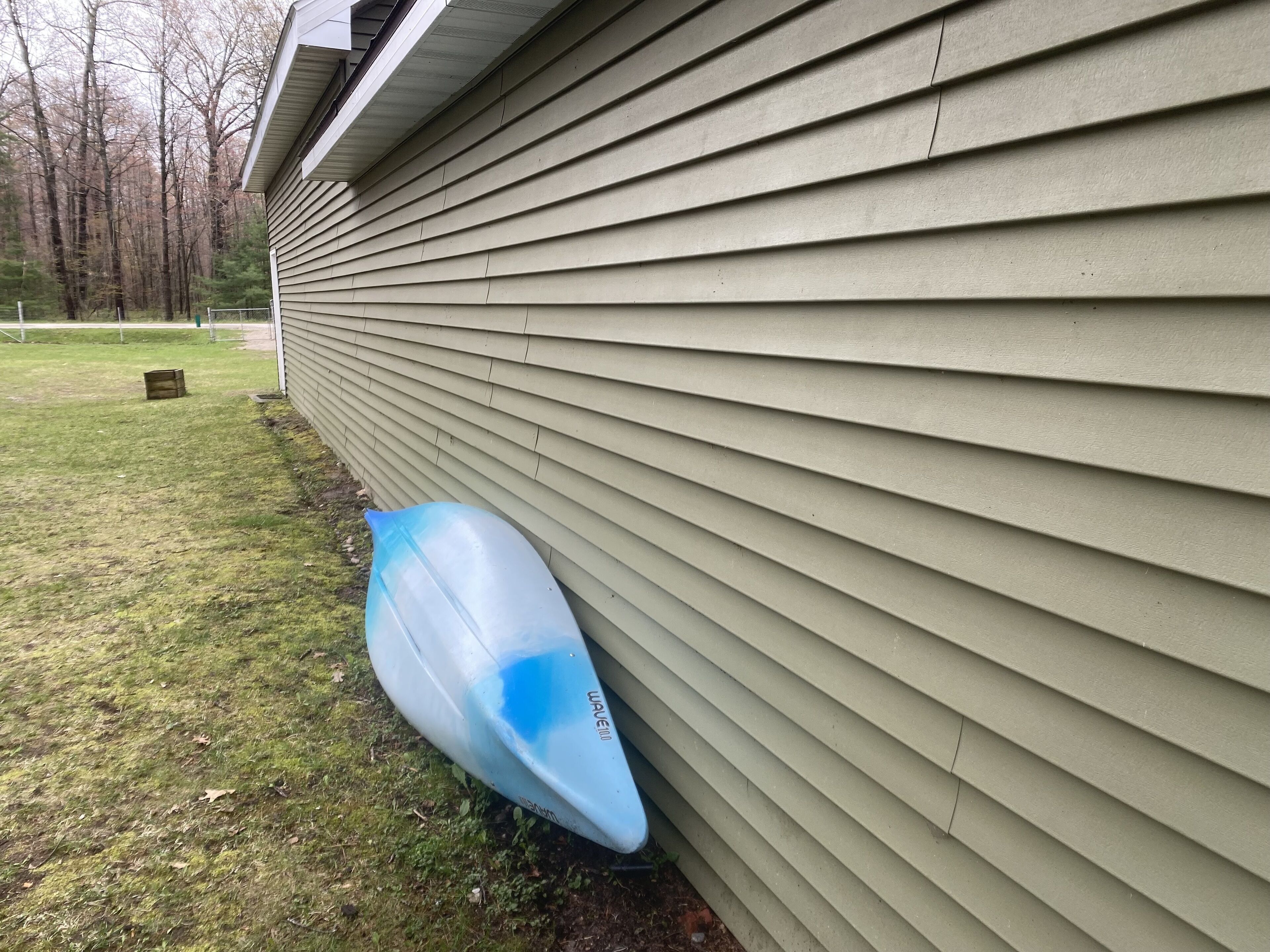A house with siding and a blue kayak leaning against it.
