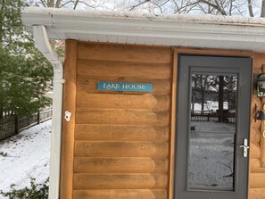 Una cabaña de madera con un letrero que dice "LAKE HOUSE" y una puerta con un ventanal.