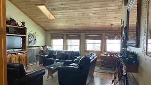 Een knusse woonkamer met een houten plafond, een televisie, een open haard en een eethoek met een tafel en stoelen.