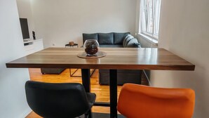 Ein moderner Essbereich mit einem Holztisch, zwei schwarzen und einem orangen Stuhl, einer Glasvase auf dem Tisch und einem grauen Sofa im Hintergrund.