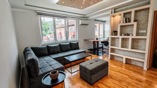 Ein modernes Wohnzimmer mit einer Eckcouch, einem kleinen runden Tisch und Holzboden.