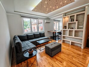 A modern living room with a sectional sofa, a small round table, and a wooden floor. - Apartman in heart of Bascarsija.To walk distance of the most city attractions. (Sarajevo)