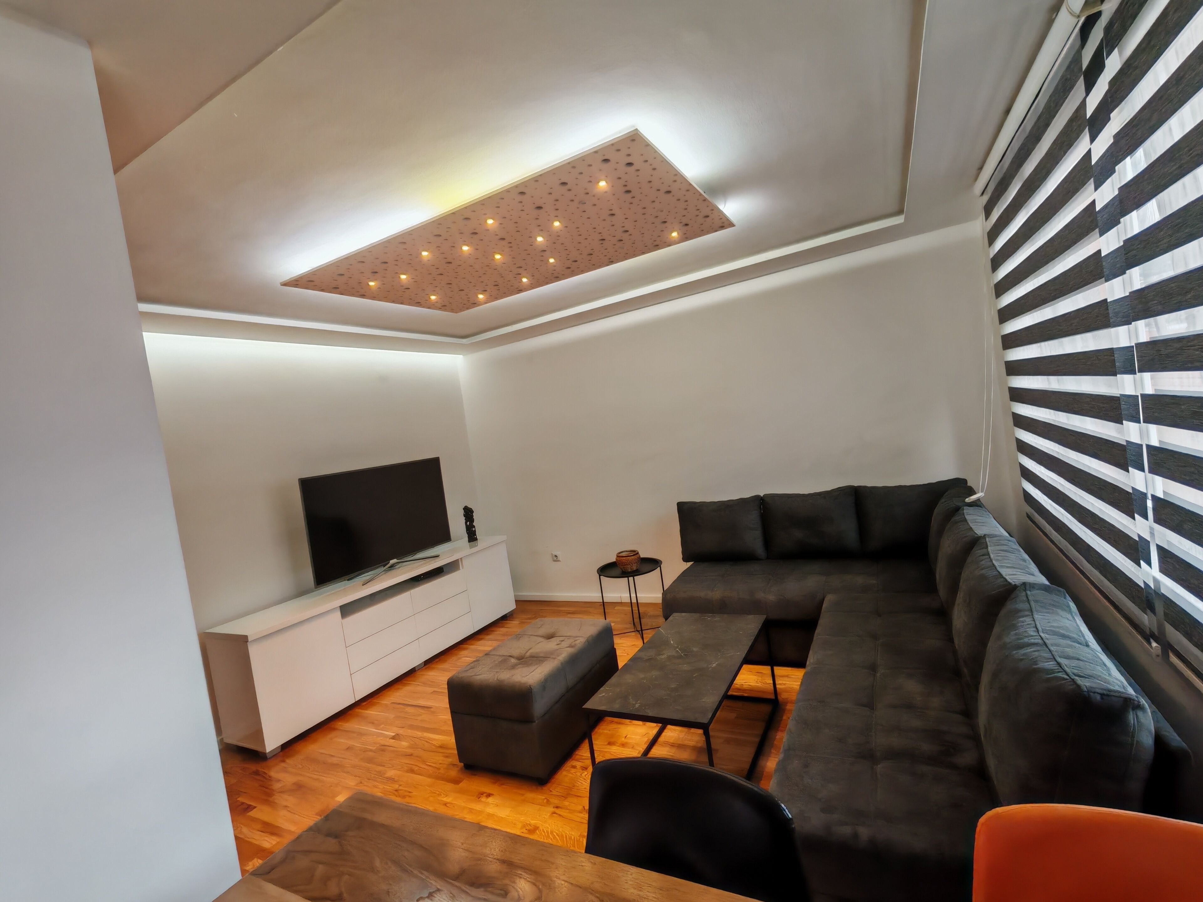 A modern living room with a sectional sofa, a flat-screen TV, a coffee table, and a small side table.