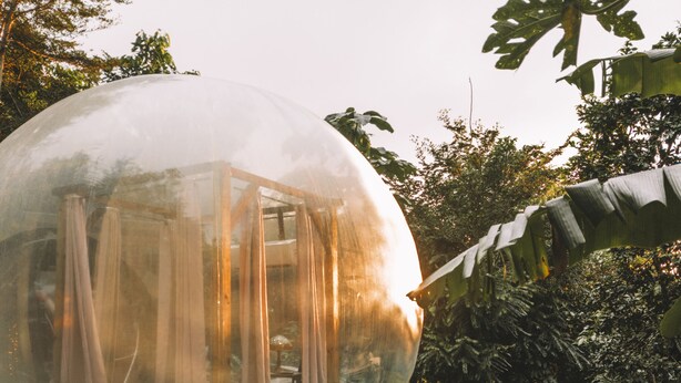 Estructura abovedada transparente con una terraza de madera y un jardín.