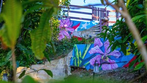 Un jardín con un mural colorido, una valla de madera y un muro de concreto.