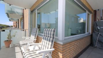 A balcony with two white chairs, a potted plant, and a barbecue grill.