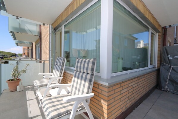 Un balcon avec deux chaises blanches, une plante en pot et un barbecue.
