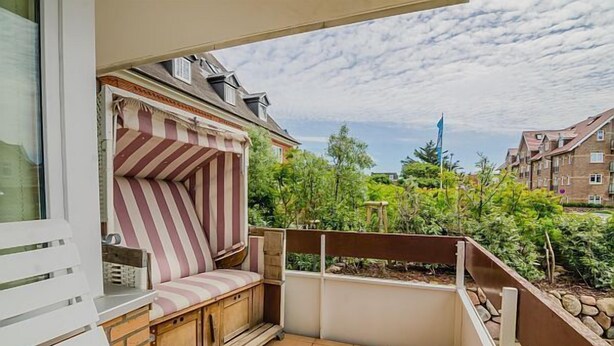 Un balcone con zona relax e cuscini a righe, vista su un quartiere residenziale e cielo sereno.