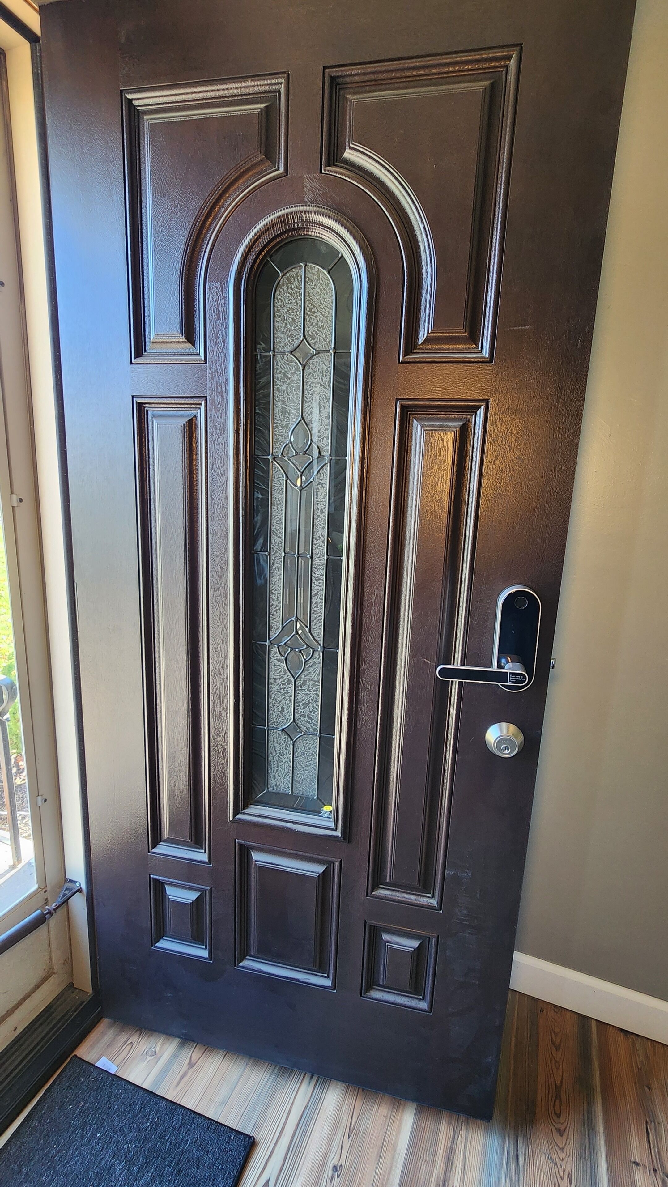 Una puerta marrón oscuro con paneles decorativos y un panel de vidrio.
