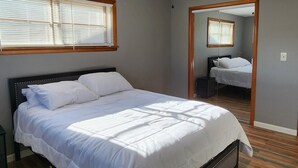 A bedroom with a bed, wooden flooring, a ceiling fan, and a window with blinds.