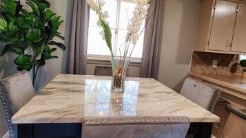 Une table de salle à manger en marbre, ornée d’un vase de fleurs blanches, entourée de chaises.
