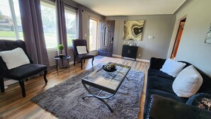 A modern living room with a dark sofa set, a glass coffee table, and a fluffy rug.