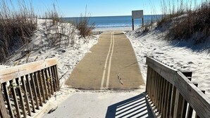 Een zandpad dat naar het strand leidt, met houten leuningen aan beide kanten.