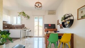 A modern kitchen with white cabinets, a dining area with a wooden table, and a green and yellow chair. - Fabula Rooms - flat - 3 Suites with 3 bathrooms (Bologna)