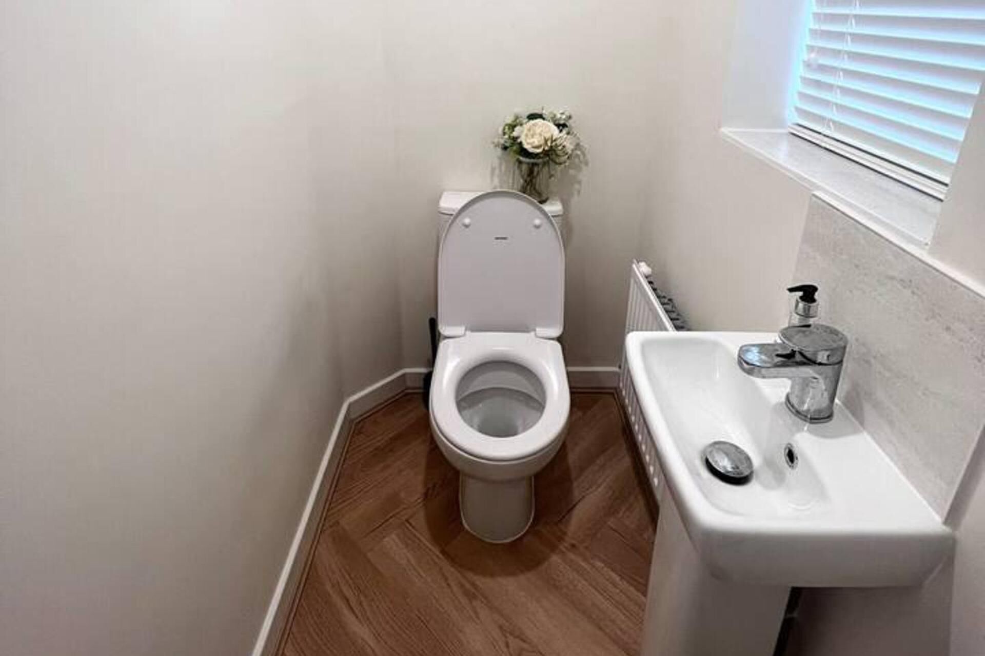 A small bathroom with a toilet, sink, and a vase with flowers on the wall.