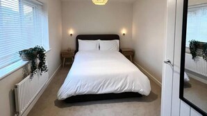 Een slaapkamer met een groot bed, twee nachtkastjes, een hanglamp en een radiator.