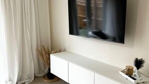 Een flatscreen televisie bevestigd aan een muur boven een witte console, met een raam en gordijnen op de achtergrond.