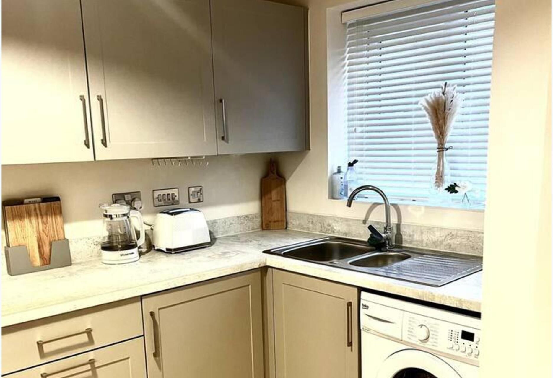 A kitchen with a washing machine, a sink, and a window with blinds.