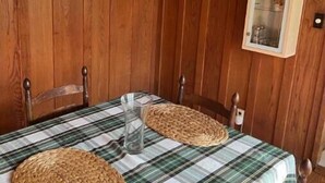 Ein Zimmer mit Holzwandverkleidung, einer karierten Tischdecke, zwei gewebten Platzsets, einem Glasbehälter und gerahmten Bildern an den Wänden.