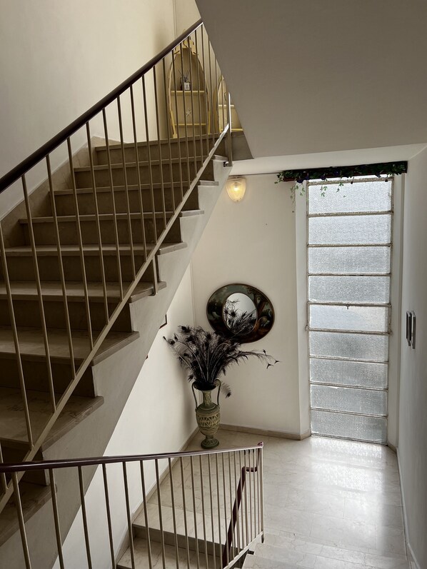 A staircase with a metal railing, a vase with decorative elements, and a wall-mounted mirror. - Hotel Till (Rimini)