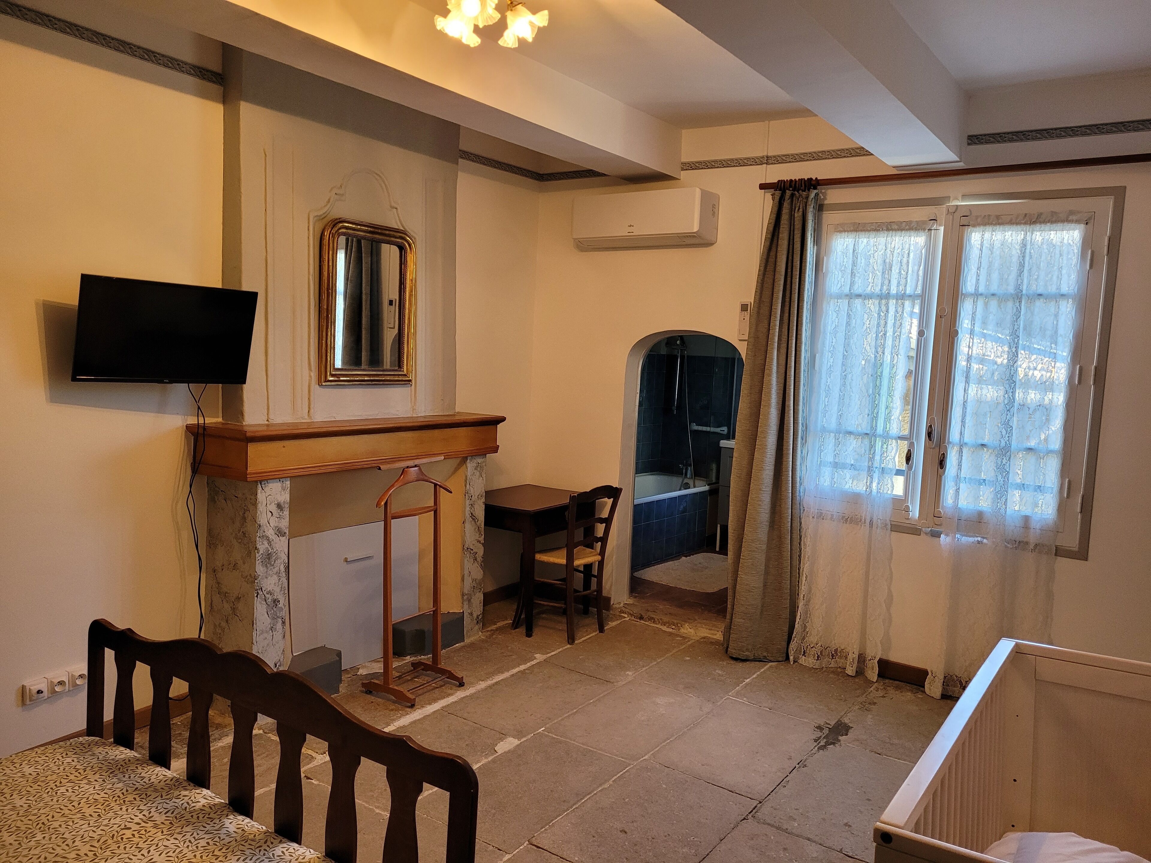 A room with a bed, a desk, a chair, a television, a mirror, and a window with curtains.