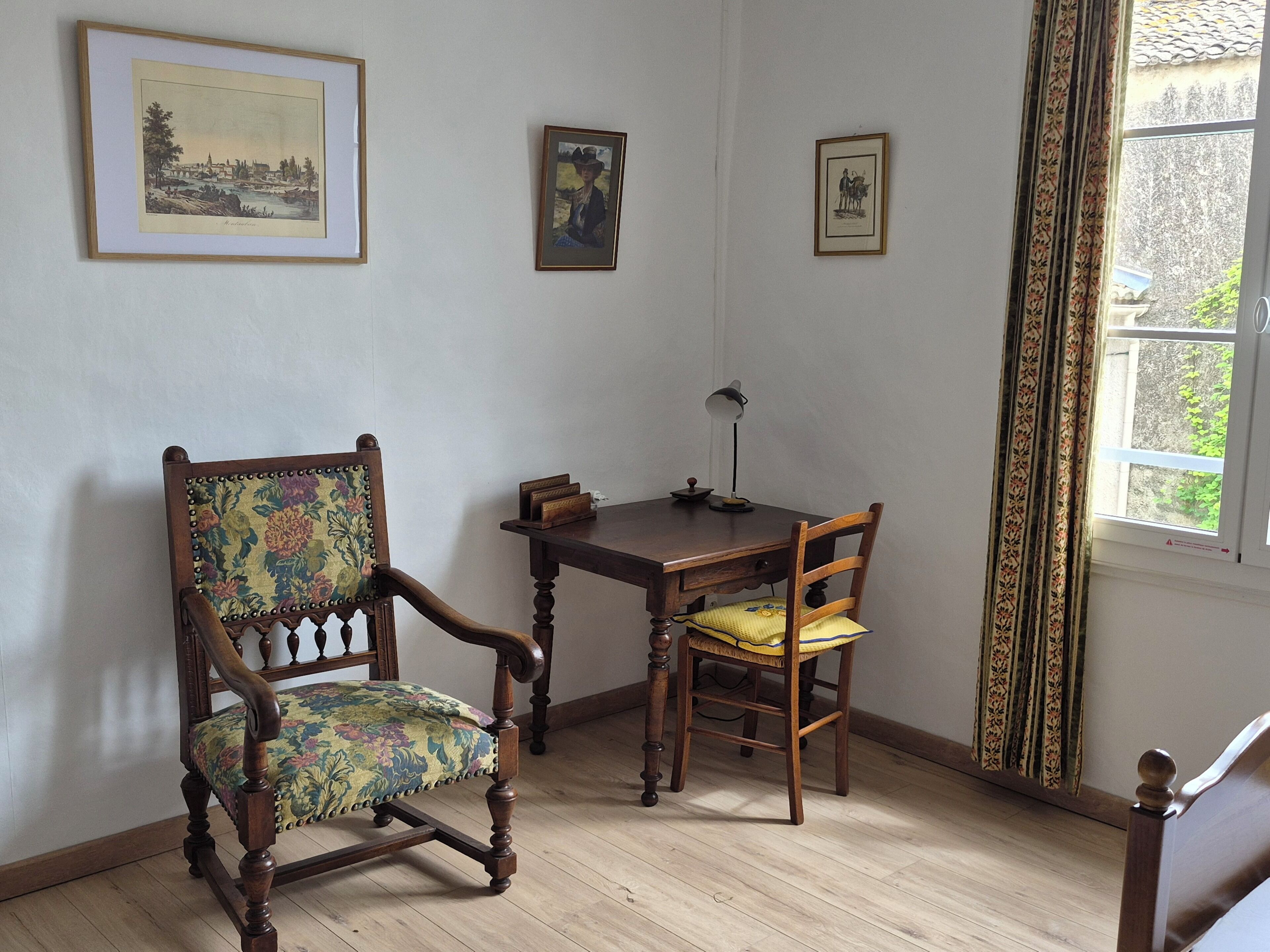 A room with a wooden chair, a wooden table, and two framed pictures on the wall.