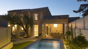 A swimming pool with lounge chairs, a patio area, and a stone building with a tiled roof.